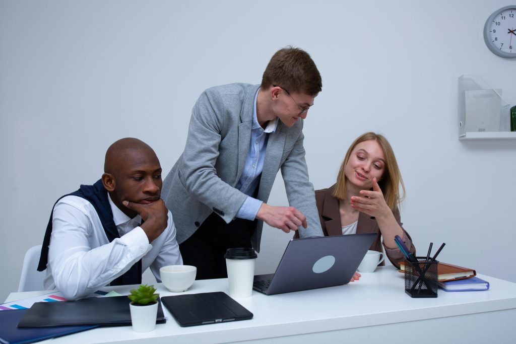 A diverse team collaborating in a modern office environment, discussing work on a laptop.