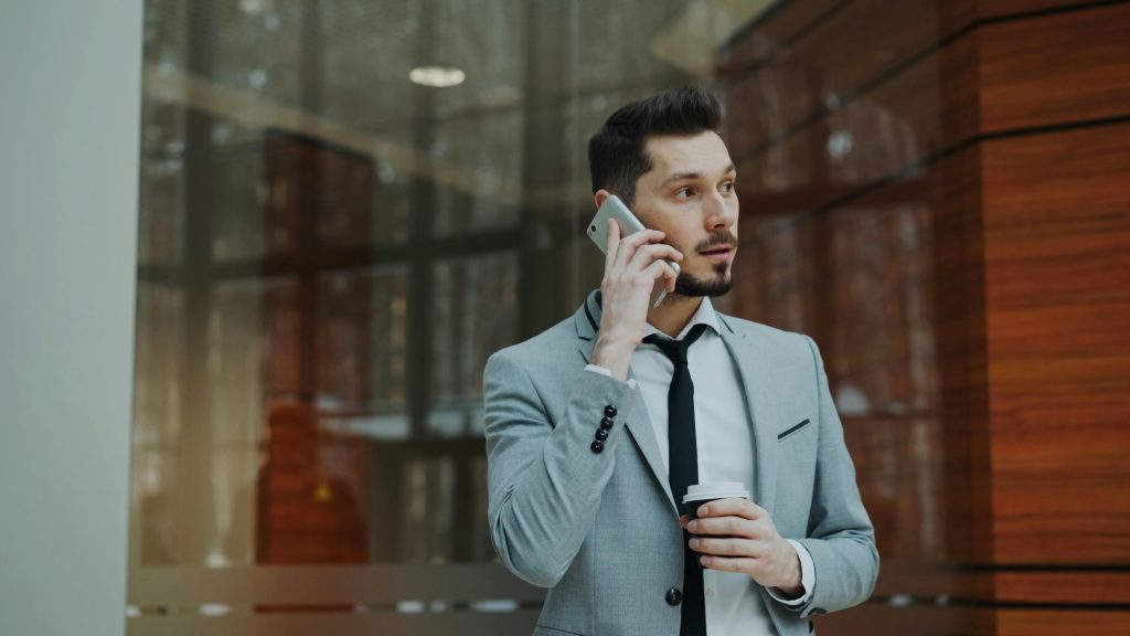 Confident businessman in gray suit conversing on smartphone indoors.